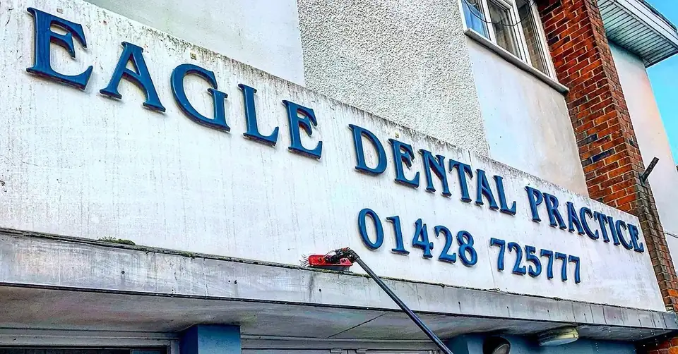 Water-fed pole cleaning the sign and glazing of a dental practice